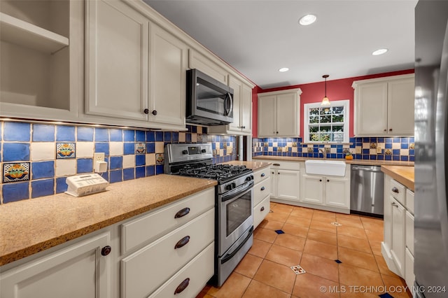 kitchen with stainless steel appliances, backsplash, sink, pendant lighting, and white cabinets