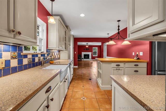 kitchen featuring decorative backsplash, white cabinets, light tile patterned floors, sink, and decorative light fixtures