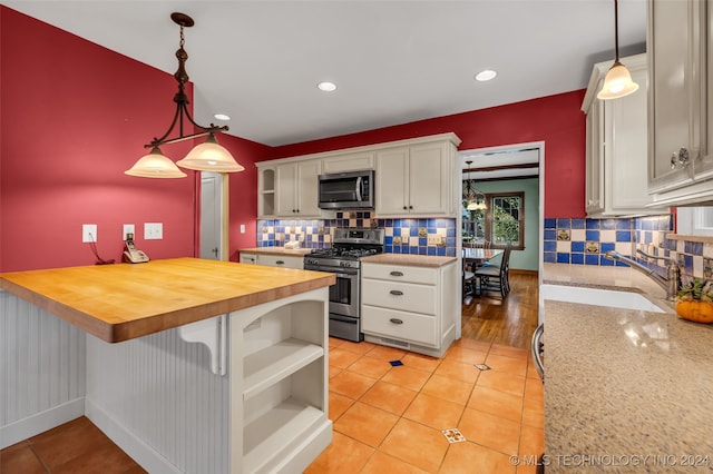 kitchen with appliances with stainless steel finishes, wood counters, white cabinets, and decorative light fixtures