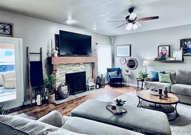 living room with a textured ceiling, a stone fireplace, hardwood / wood-style flooring, and ceiling fan