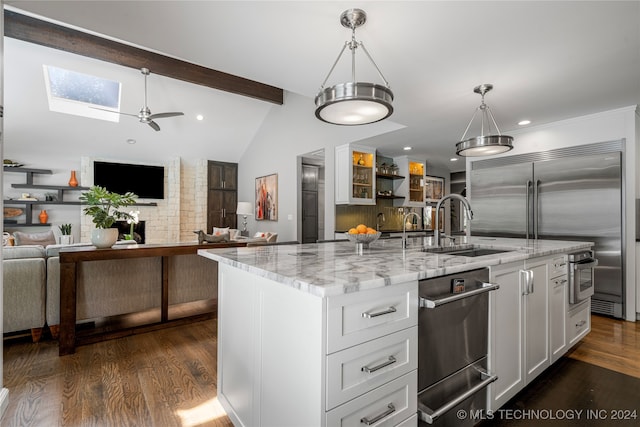 kitchen with hanging light fixtures, a center island with sink, lofted ceiling with skylight, white cabinets, and light stone counters