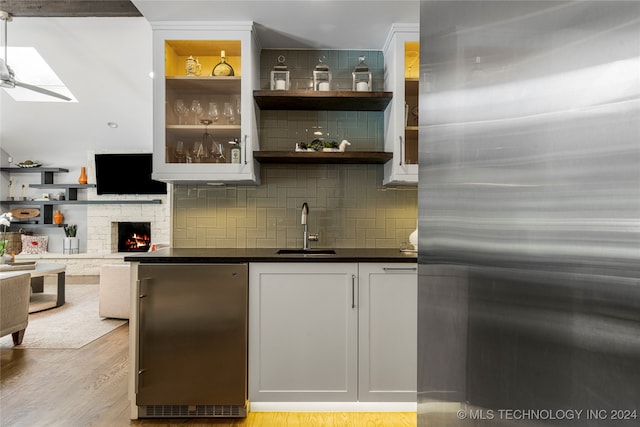 bar with sink, light wood-type flooring, a fireplace, white cabinets, and stainless steel refrigerator