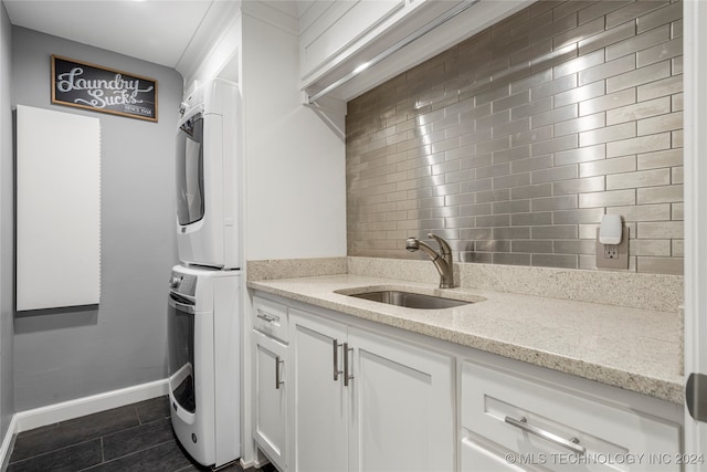 washroom with dark tile patterned floors, sink, and stacked washer and clothes dryer