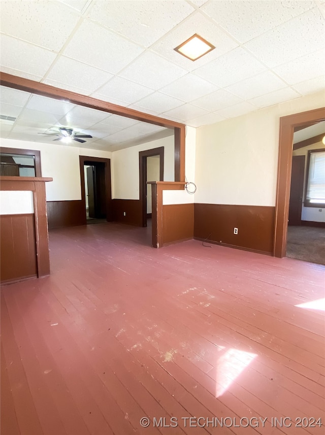 empty room featuring a paneled ceiling, wood walls, wood-type flooring, and ceiling fan