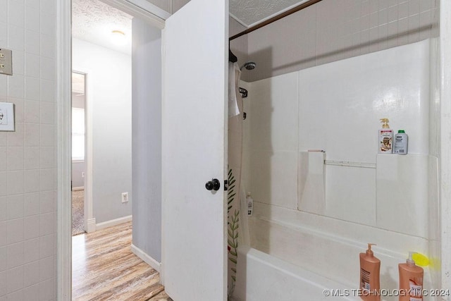 full bath featuring baseboards, bathing tub / shower combination, and wood finished floors