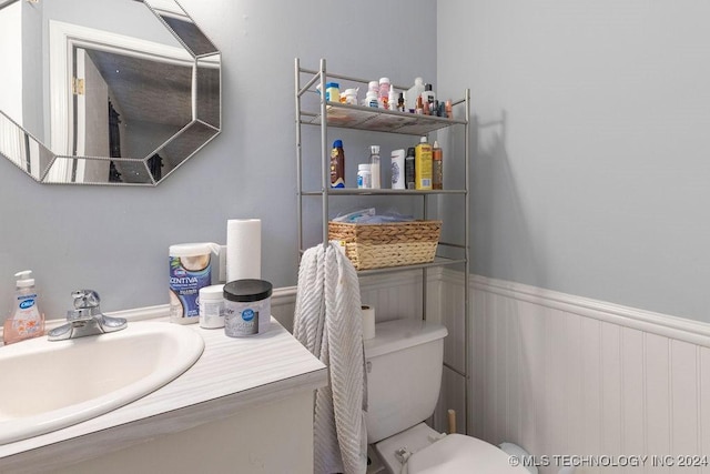 bathroom featuring vanity, toilet, and a wainscoted wall