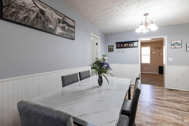 dining area featuring a textured ceiling, wood finished floors, wainscoting, and a notable chandelier