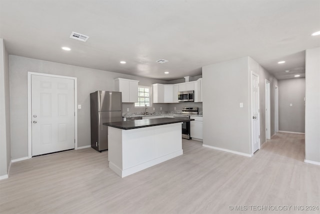 kitchen with sink, a kitchen island, white cabinetry, stainless steel appliances, and light hardwood / wood-style flooring