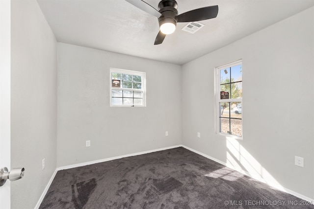 unfurnished room featuring a wealth of natural light, dark colored carpet, and ceiling fan