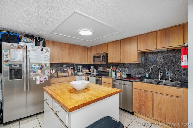 kitchen with wood counters, light tile patterned flooring, stainless steel appliances, sink, and a center island