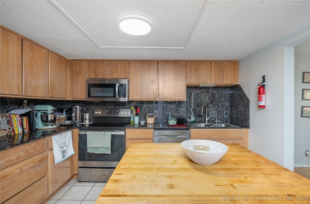 kitchen featuring sink, a textured ceiling, stainless steel appliances, wooden counters, and decorative backsplash