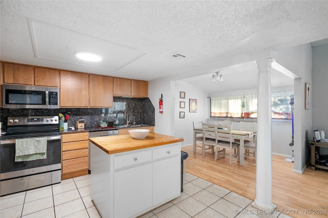 kitchen featuring lofted ceiling, a kitchen island, appliances with stainless steel finishes, butcher block counters, and light tile patterned flooring