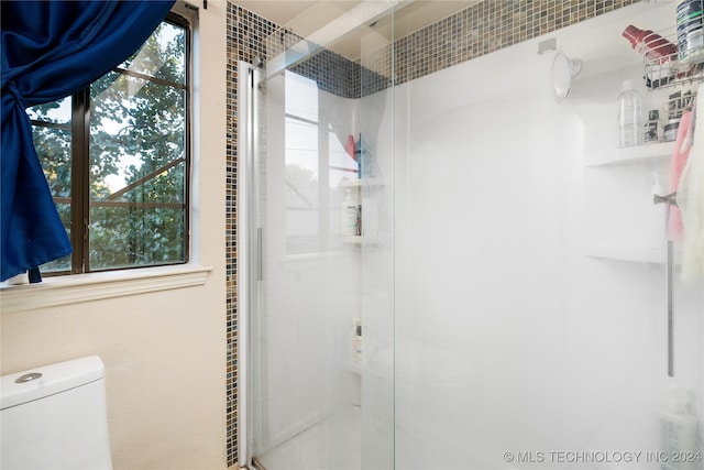 bathroom with toilet, a healthy amount of sunlight, and a shower with shower door