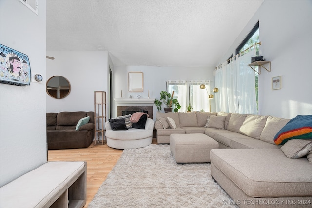 living room featuring a textured ceiling, hardwood / wood-style flooring, a tiled fireplace, and vaulted ceiling