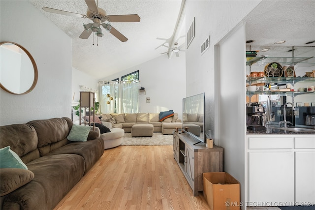 living room with light hardwood / wood-style flooring, a textured ceiling, sink, and vaulted ceiling