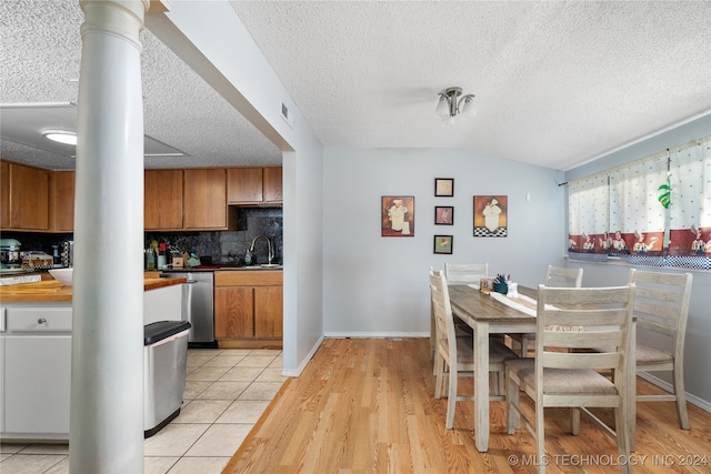 kitchen featuring tasteful backsplash, stainless steel dishwasher, vaulted ceiling, ornate columns, and light hardwood / wood-style floors