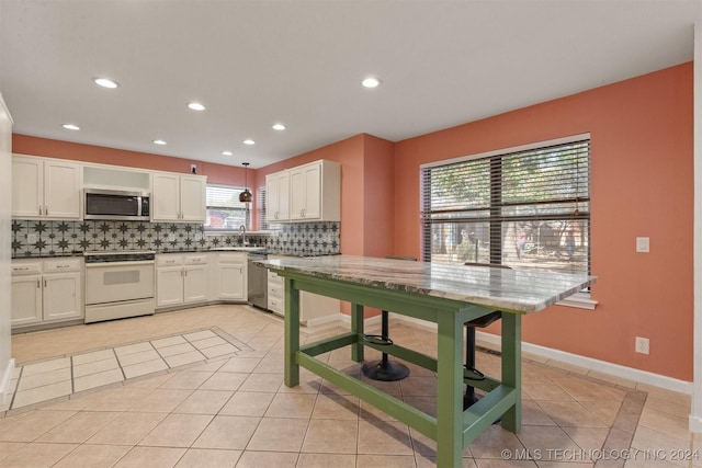 kitchen featuring kitchen peninsula, backsplash, white cabinetry, light tile patterned floors, and stainless steel appliances