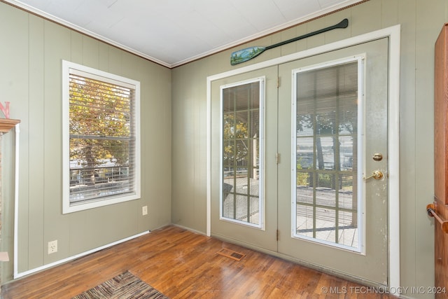 doorway to outside with wood walls, wood-type flooring, crown molding, and plenty of natural light