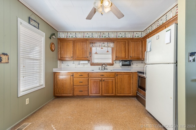 kitchen featuring white refrigerator, stainless steel stove, wood walls, sink, and ceiling fan