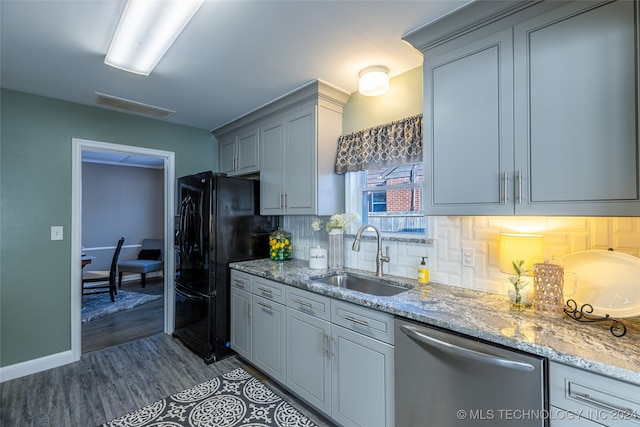 kitchen featuring black refrigerator, backsplash, sink, light stone countertops, and stainless steel dishwasher