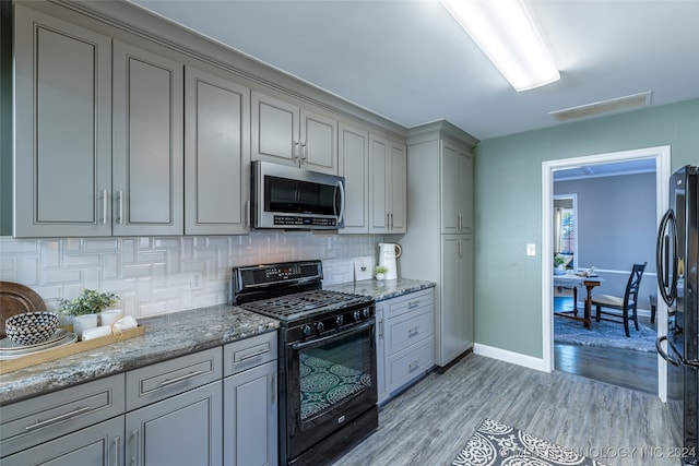 kitchen with decorative backsplash, black appliances, gray cabinets, light hardwood / wood-style floors, and stone counters