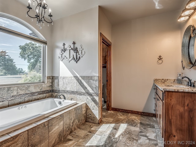 bathroom with vanity, a healthy amount of sunlight, an inviting chandelier, and tiled tub