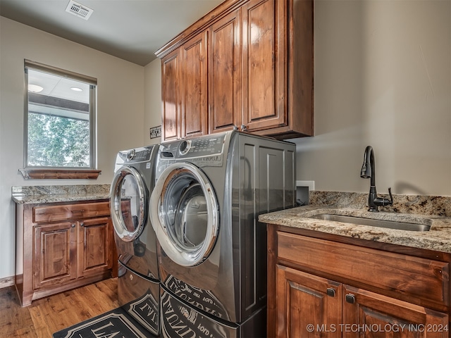 laundry area featuring cabinets, sink, washer and clothes dryer, and light hardwood / wood-style floors