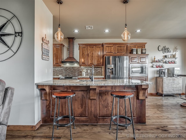 kitchen featuring wall chimney range hood, a breakfast bar area, kitchen peninsula, stainless steel appliances, and wood-type flooring