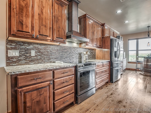 kitchen with light stone countertops, wall chimney range hood, appliances with stainless steel finishes, light hardwood / wood-style floors, and decorative backsplash