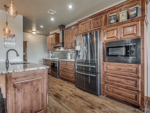 kitchen featuring wall chimney range hood, appliances with stainless steel finishes, dark hardwood / wood-style floors, pendant lighting, and sink