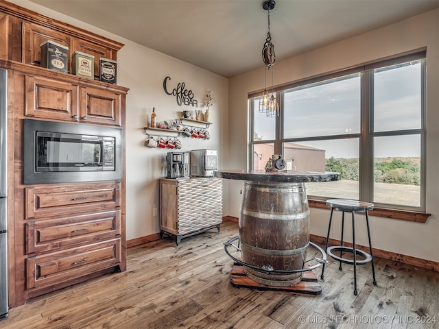 bar with a wealth of natural light, pendant lighting, light hardwood / wood-style flooring, and stainless steel microwave