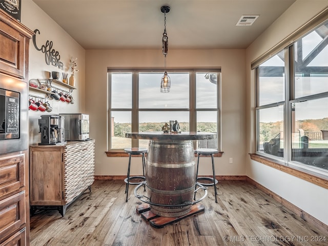 bar with light hardwood / wood-style flooring, decorative light fixtures, and stainless steel microwave