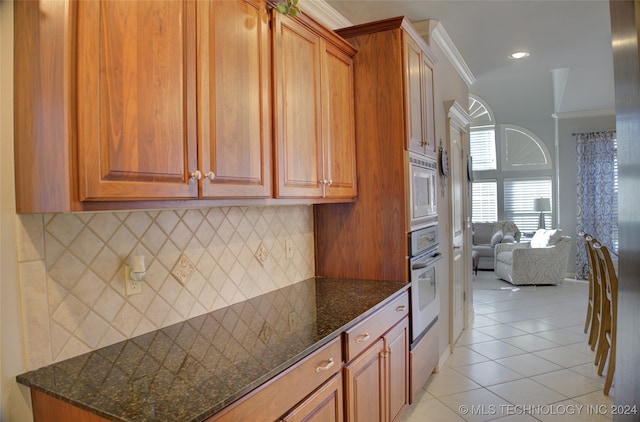 kitchen featuring backsplash, dark stone countertops, light tile patterned flooring, appliances with stainless steel finishes, and ornamental molding