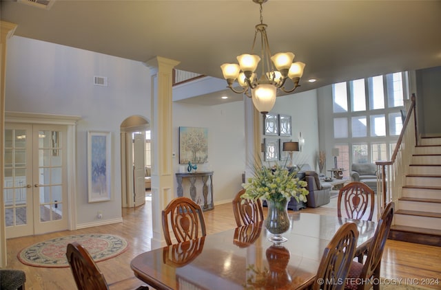 dining area with a high ceiling, ornate columns, french doors, a notable chandelier, and light hardwood / wood-style flooring