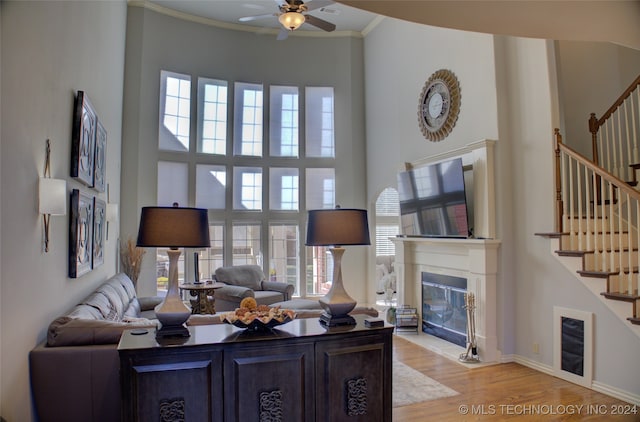 living room with ceiling fan, a towering ceiling, crown molding, and light hardwood / wood-style floors