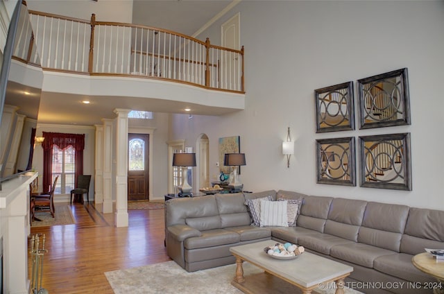 living room featuring decorative columns, ornamental molding, a towering ceiling, and light wood-type flooring