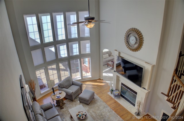 living room featuring a tiled fireplace, light hardwood / wood-style floors, a towering ceiling, and a healthy amount of sunlight