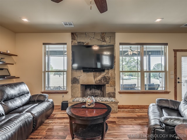 living room featuring ceiling fan, hardwood / wood-style flooring, and a stone fireplace