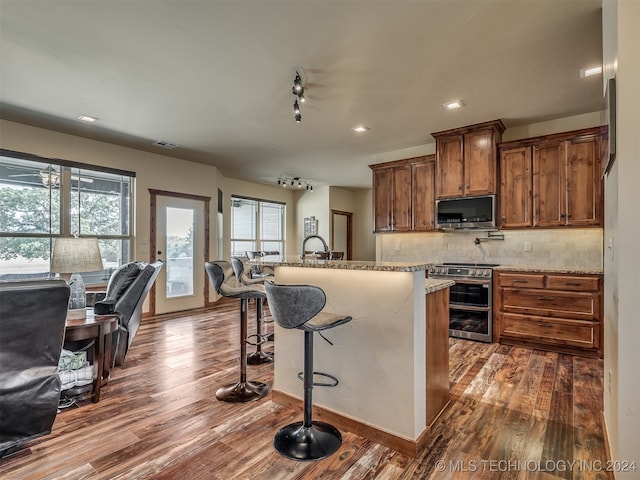 kitchen with a kitchen breakfast bar, stainless steel appliances, backsplash, light stone countertops, and dark hardwood / wood-style flooring