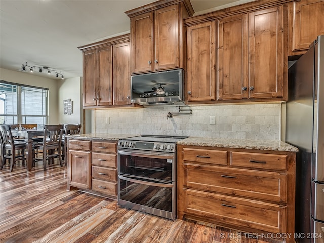 kitchen featuring light stone countertops, appliances with stainless steel finishes, rail lighting, dark wood-type flooring, and decorative backsplash