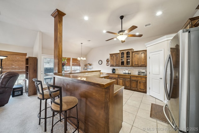 kitchen with ornate columns, vaulted ceiling, a breakfast bar, pendant lighting, and stainless steel refrigerator