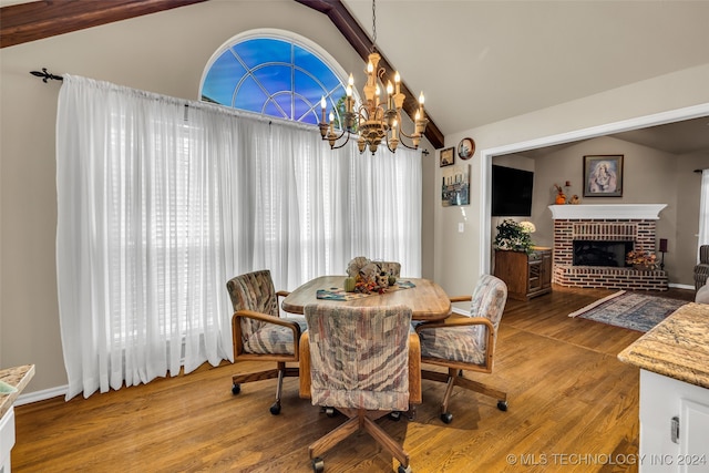 dining space featuring an inviting chandelier, wood-type flooring, vaulted ceiling, and a brick fireplace