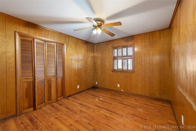 unfurnished bedroom featuring wooden walls, light hardwood / wood-style flooring, a closet, and ceiling fan