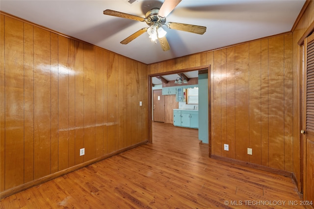 spare room featuring light hardwood / wood-style floors, wooden walls, sink, and ceiling fan