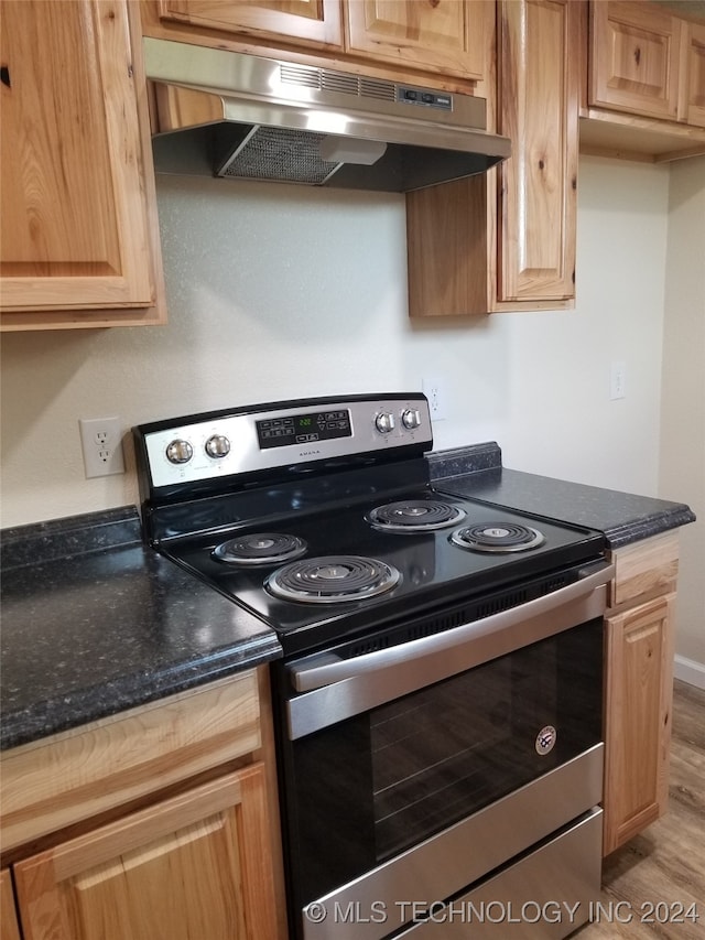 kitchen with stainless steel range with electric stovetop, light hardwood / wood-style flooring, and dark stone counters