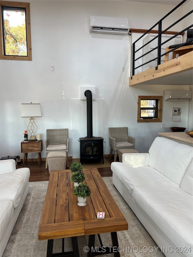 living area with an AC wall unit, wood finished floors, and a wood stove