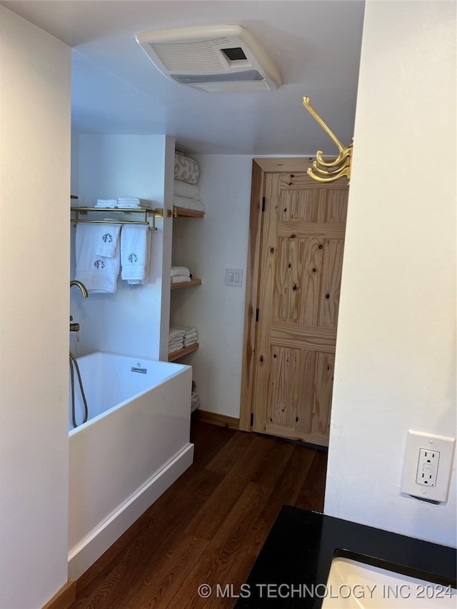 bathroom featuring visible vents, baseboards, wood finished floors, and a bath