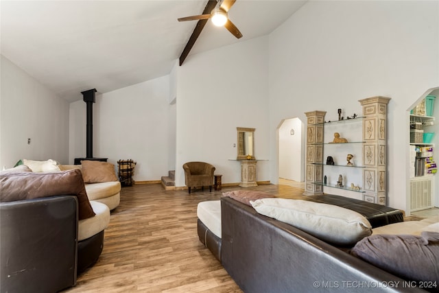 living room featuring beam ceiling, ceiling fan, high vaulted ceiling, light hardwood / wood-style flooring, and a wood stove