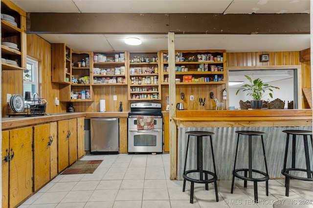 kitchen featuring a kitchen breakfast bar, wooden walls, stainless steel appliances, and light tile patterned floors