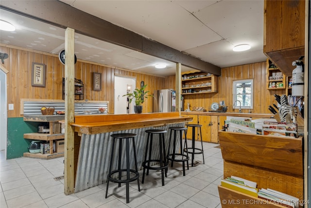 kitchen with wooden walls, stainless steel refrigerator, light tile patterned flooring, and a kitchen bar